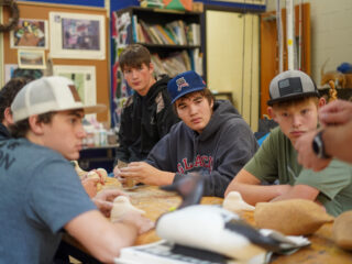 High school students around a table, listening to a teacher