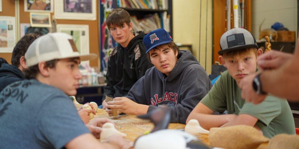 High school students around a table, listening to a teacher